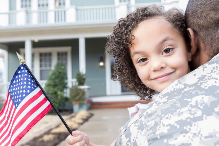 Girl hugging father holding american flag in front of home