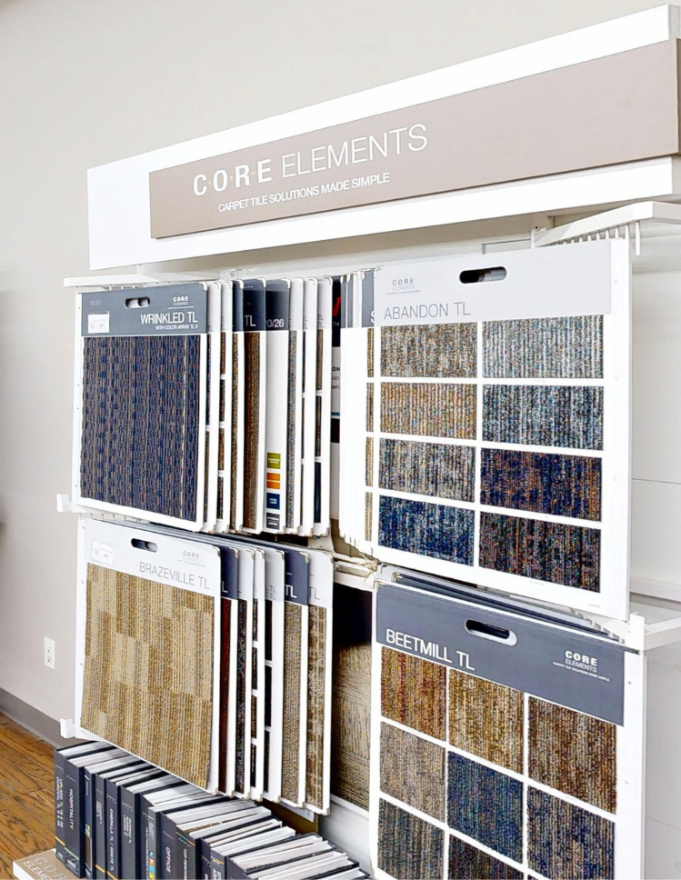 Display rack with multiple carpet samples of various colors and patterns, labeled with brand names like Core Elements, Brandon TL, and Beetmill TL.