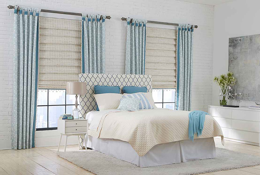 Bedroom with white and blue curtains, bed, bedspread, and pillows on a white rug and floors.